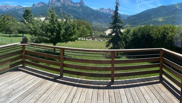 A wooden deck with a railing overlooking a mountainous landscape.