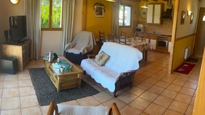 A living room with a sofa, armchair, coffee table, television, and dining area with chairs and a table.