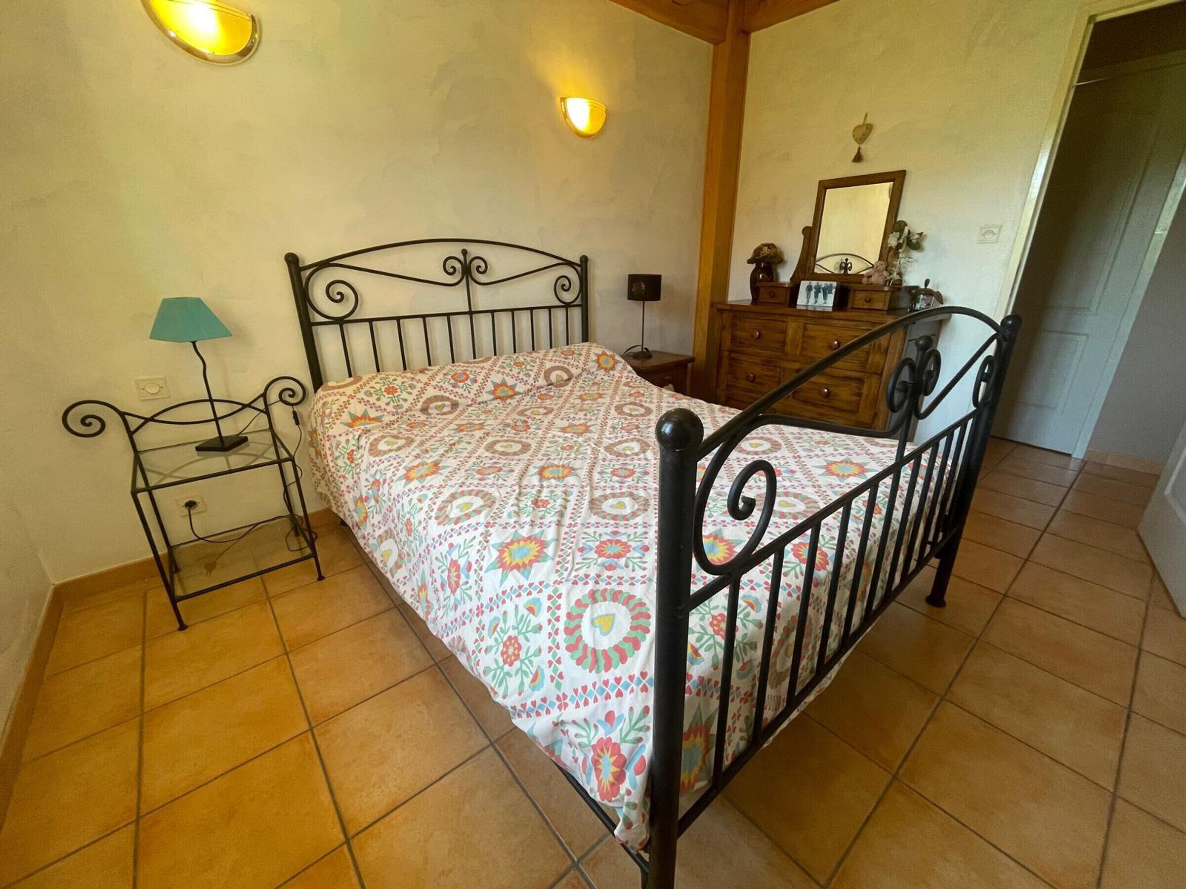 A room with a bed, a nightstand, a lamp, a dresser, and a mirror.