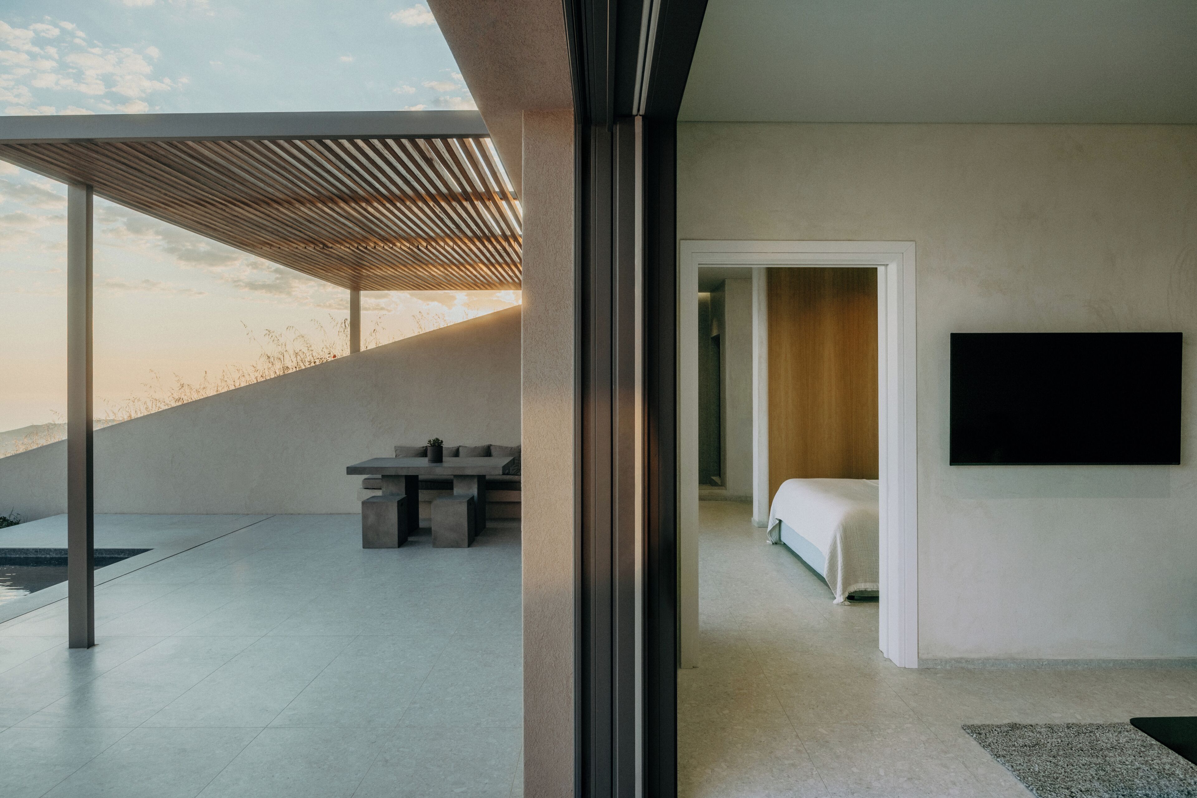 A modern interior with a minimalist design, featuring a large window, a flat-screen TV mounted on the wall, and a simple bed setup.