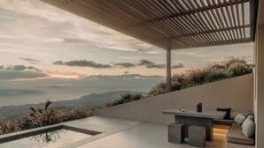 A modern outdoor patio with a minimalist design, a seating area, and a view of the landscape. - Santorini Sky, Luxury Resort (Santorini)