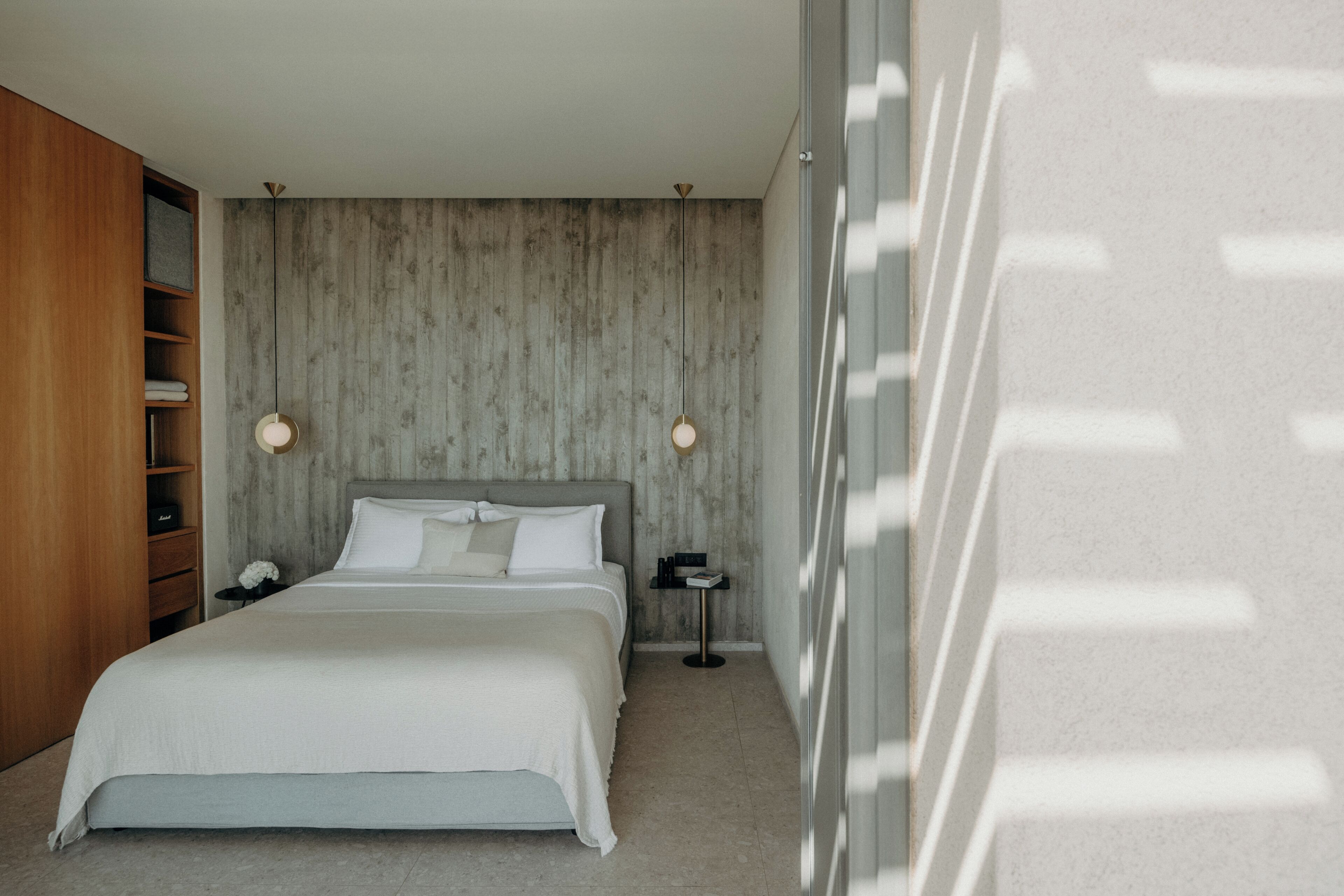 A modern bedroom with a large bed, wooden wardrobe, and a concrete wall.