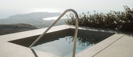 A modern outdoor pool with a metal ladder, surrounded by a concrete deck and overlooking a scenic landscape.