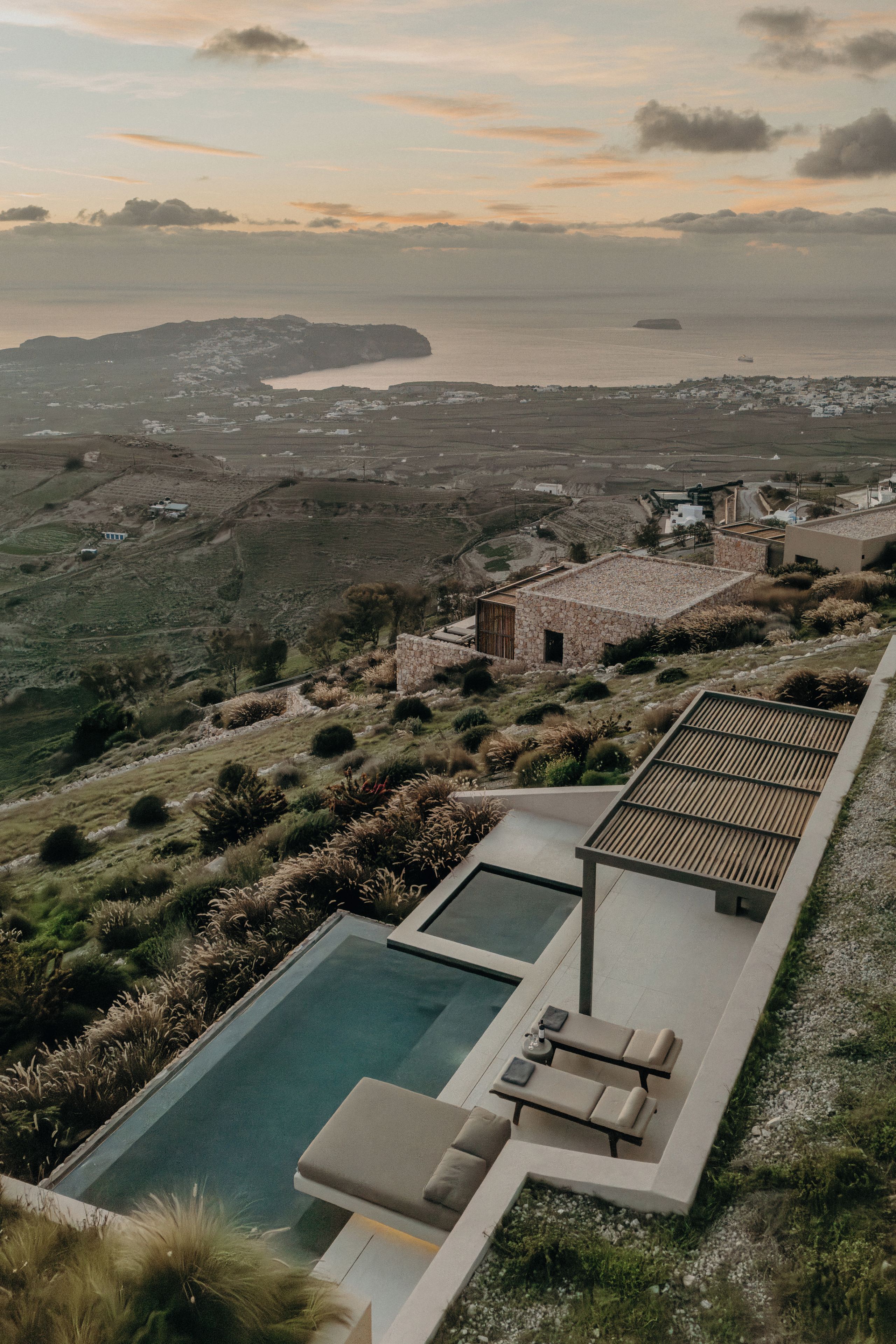 A pool area with lounge chairs and a stone building, overlooking a coastal landscape.