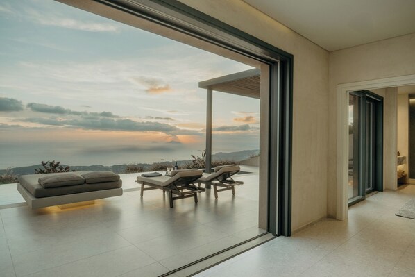 Un interior moderno con un gran ventanal corredera que da a un balcón con vistas al cielo y montañas distantes.