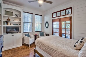 Une chambre à coucher avec un lit, une chaise, un téléviseur, une bibliothèque et une fenêtre avec des stores.