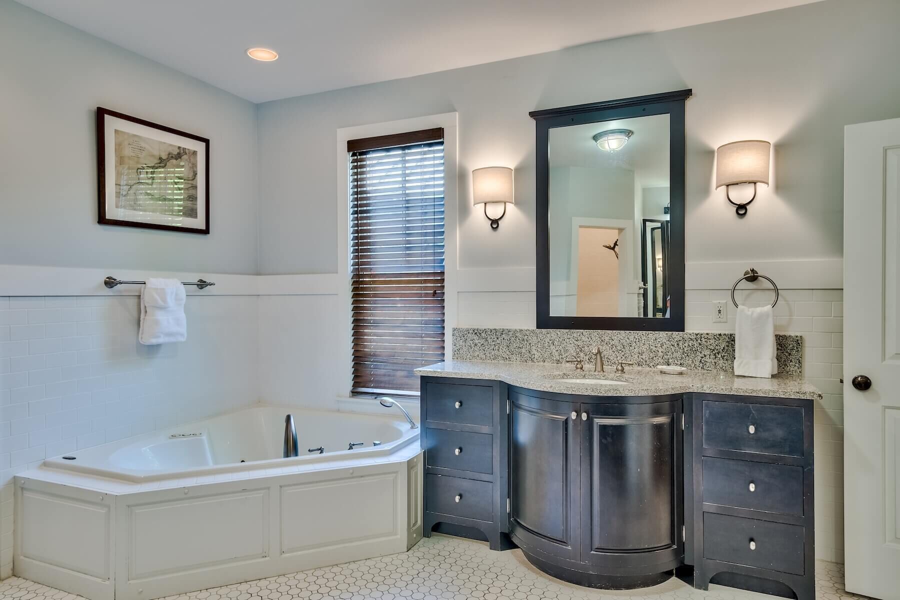A modern bathroom with a freestanding bathtub, a large vanity with a mirror, and a window with blinds.