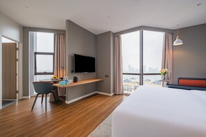 A modern hotel room with a large bed, a desk with a flat-screen TV, a chair, and a view of the city through large windows. - Holiday Inn Express Nanning Jiangnan by IHG (Nanning)