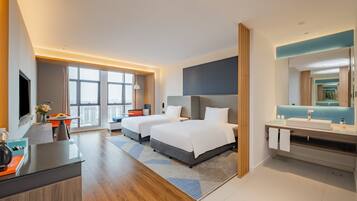 A modern hotel room with a large bed, a desk, a bathroom with a mirror, and a view of the city.