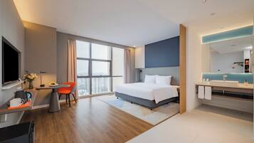 A modern hotel room with a large bed, a desk, a TV, and a bathroom with a mirror and sink.