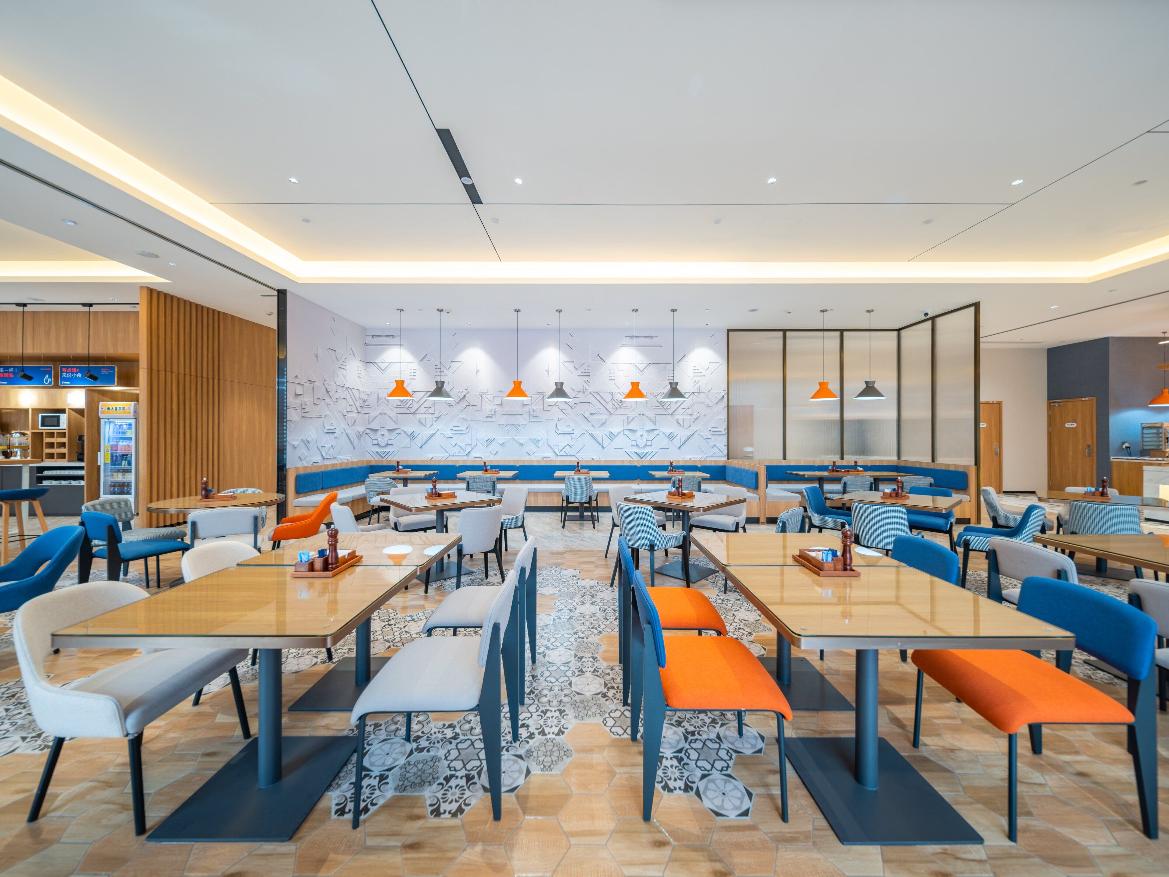 A modern dining area with multiple tables and chairs, a patterned floor, and a wall with geometric designs.