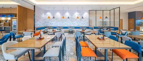 A modern dining area with multiple tables and chairs, a patterned floor, and a wall with geometric designs.