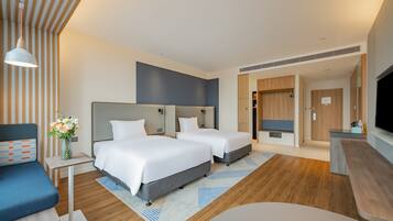 A modern hotel room with two beds, a desk, a TV, and a seating area.