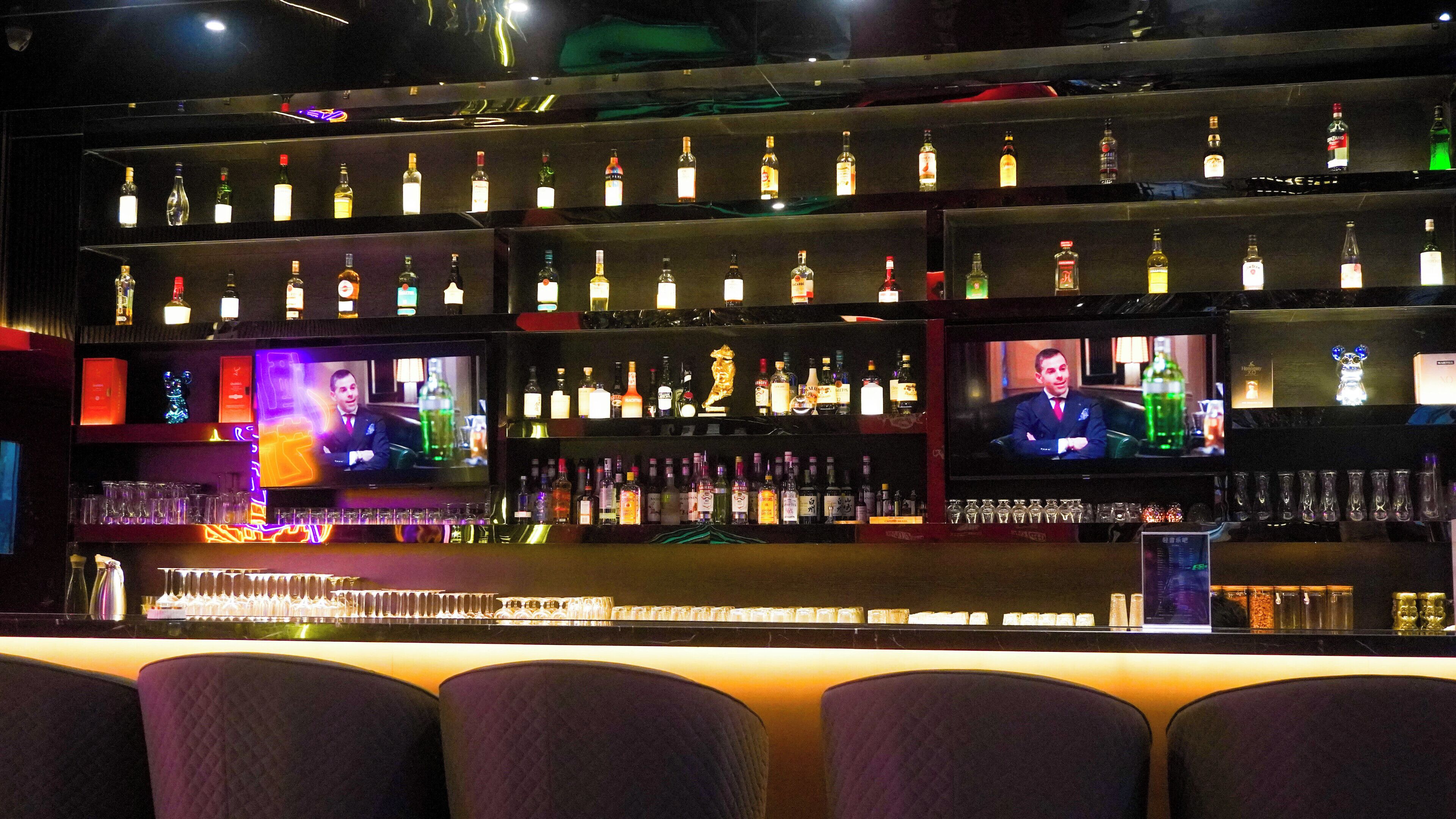 A bar with multiple shelves of liquor bottles and a television screen displaying a show.