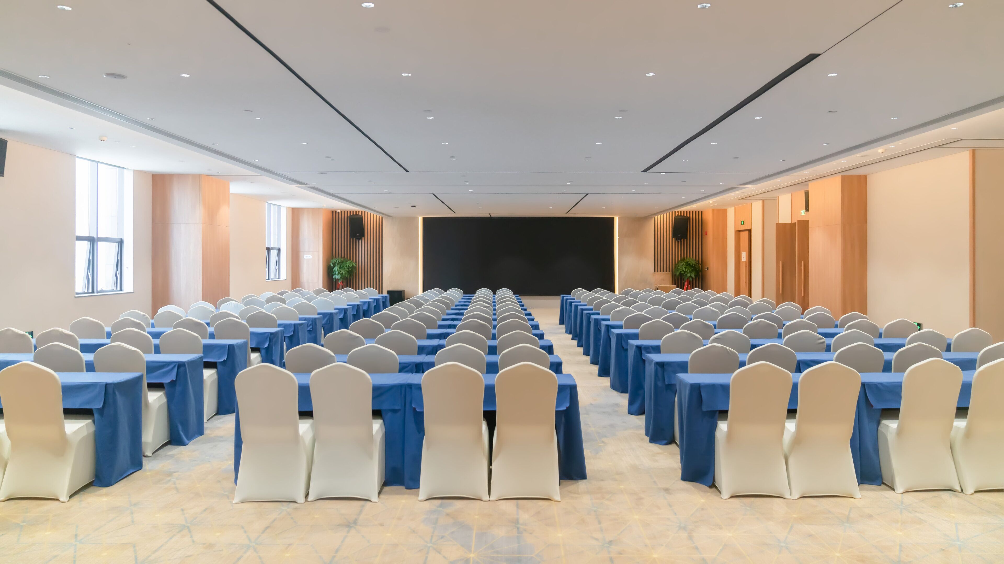 A conference room with rows of tables and chairs, a large screen at the front, and windows on one side.