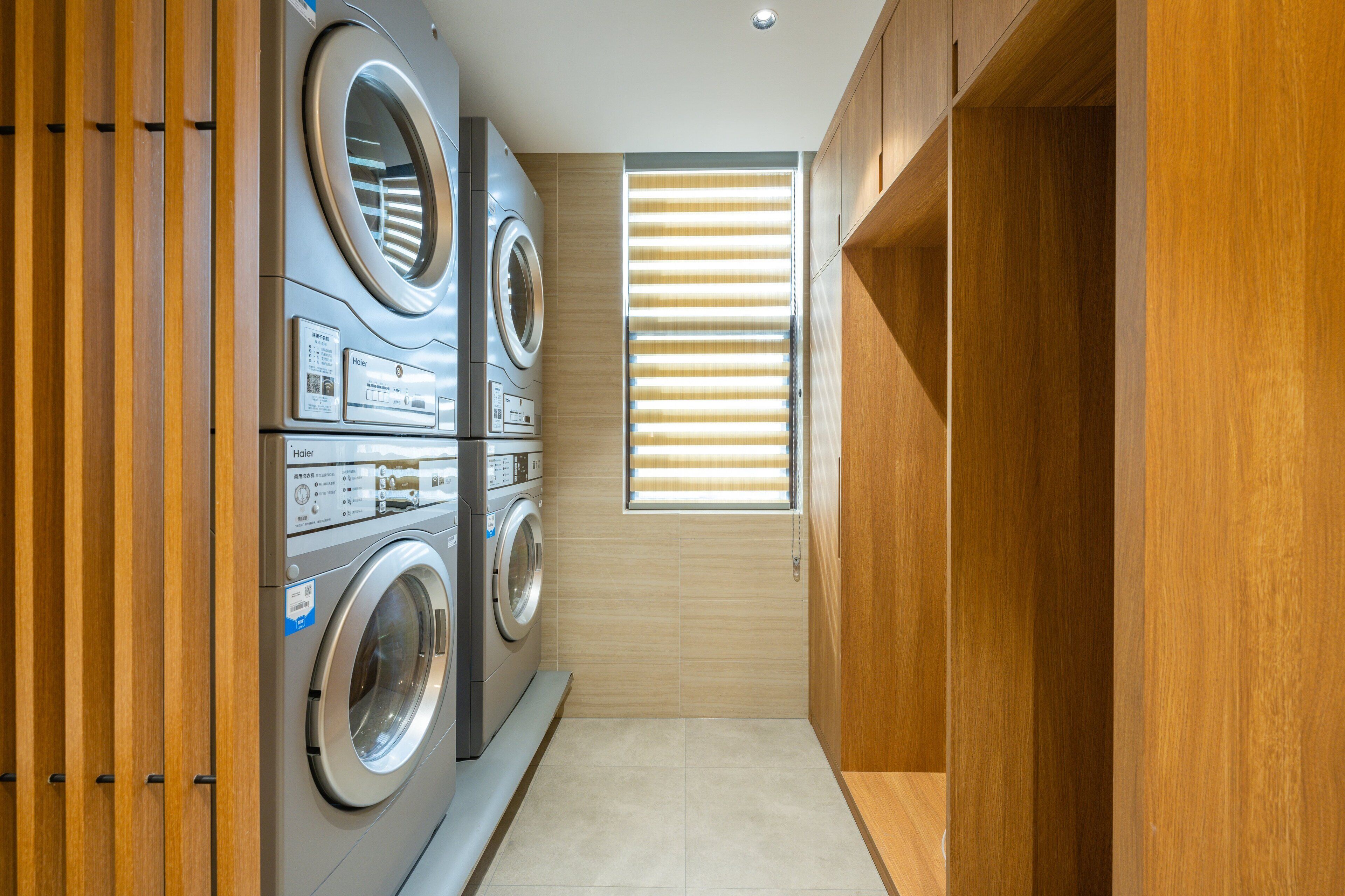 A laundry room with two front-loading washing machines and a window with blinds.