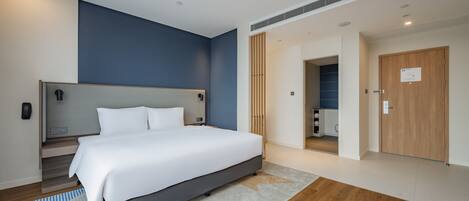 Una habitación de hotel moderna con una cama grande, una mesita de noche, un armario empotrado y un baño visible a través de una puerta abierta.