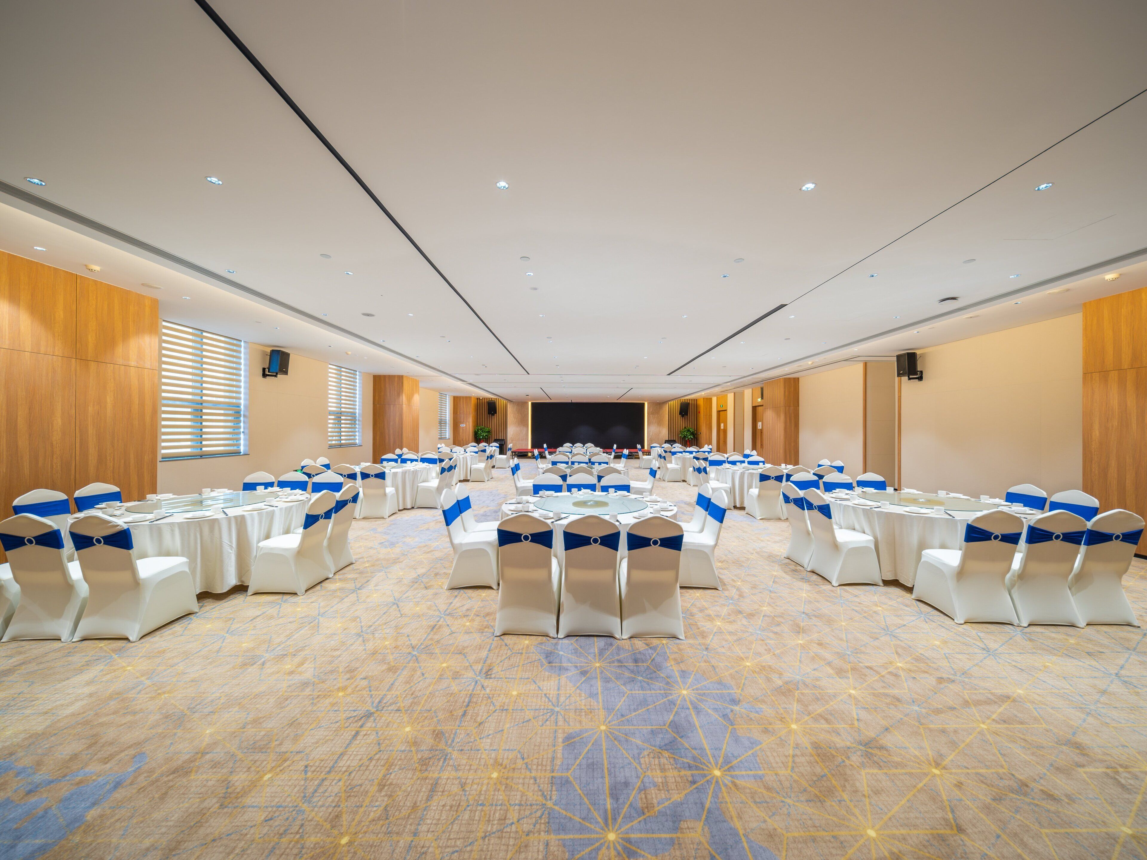 A conference room with rows of tables and chairs, a stage at the front, and wooden paneling on the walls.