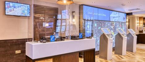 A reception area with a reception desk, a large digital map display, and self-service kiosks.