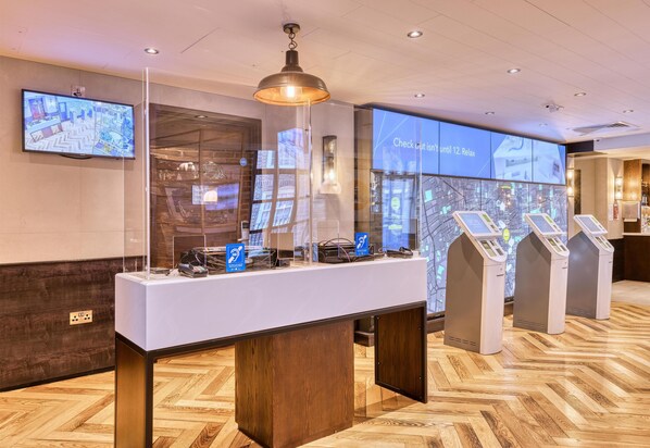 A reception area with a reception desk, a large digital map display, and self-service kiosks. - Hub By Premier Inn London Shoreditch (London)