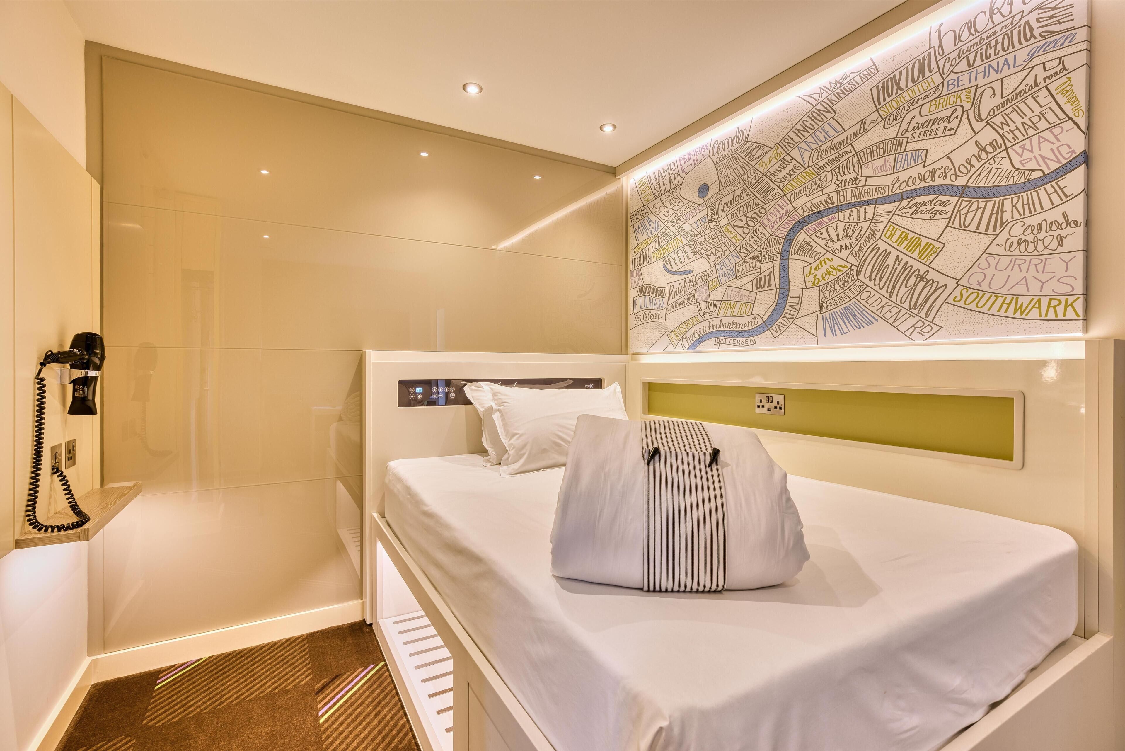 A hotel room with a bed, a map on the wall, a phone, and a small desk area.