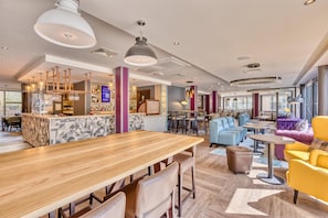 Un interior moderno con una zona de bar, diferentes disposiciones de asientos y una variedad de mesas y sillas.