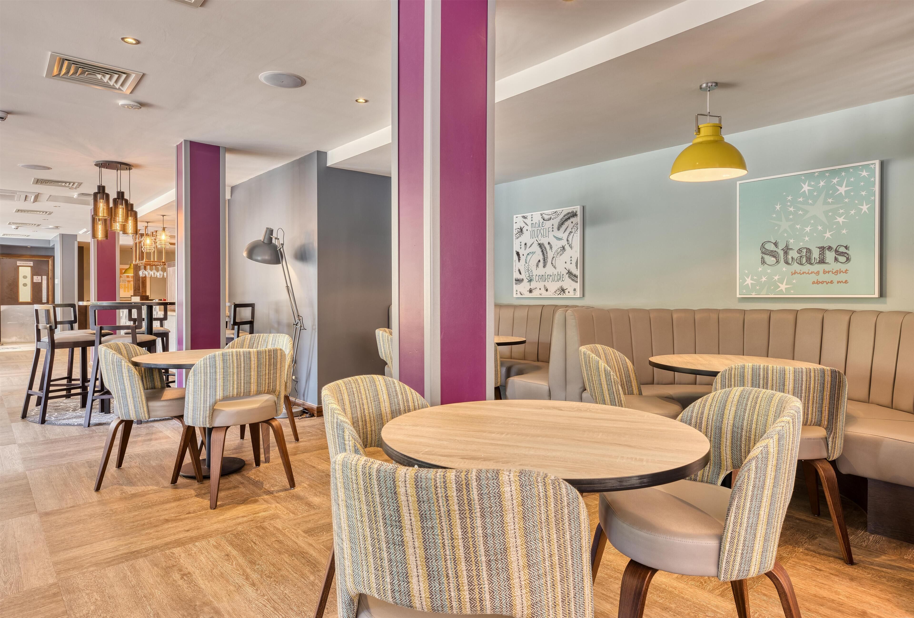 Ein modernes Interieur mit runden Tischen, gestreiften Stühlen und einer Sitzgelegenheit mit Bank sowie Wandbildern.