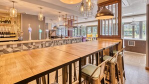 A bar area with a long wooden counter, multiple hanging light fixtures, and a bar stocked with bottles. - Premier Inn Oxford City Centre - Westgate (Oxford)