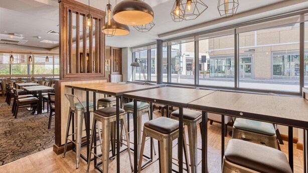 A modern restaurant with high ceilings, large windows, and a mix of bar stools and tables. - Premier Inn Oxford City Centre - Westgate (Oxford)