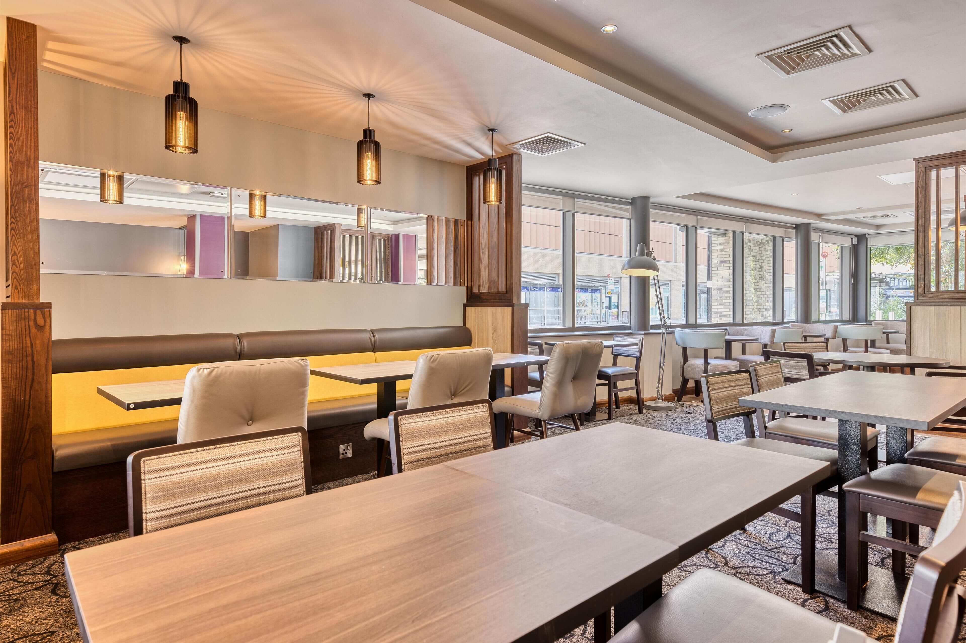 A modern dining area with booths and tables, large windows, and pendant lighting.