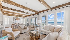 Un vaste salon doté d’une grande fenêtre donnant sur la plage, de poutres en bois au plafond et d’une table basse en verre au design original.