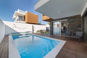 Ein moderner Poolbereich mit einem klaren, blauen Pool, einer überdachten Sitzgelegenheit und Blick auf ein benachbartes Gebäude.