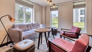 Una sala moderna con sofá, reposapiés y sillones, una mesa redonda y una lámpara de pie.