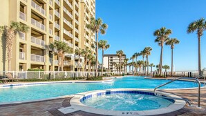 Un espace piscine d’hôtel comprenant un jacuzzi, des palmiers et un immeuble à plusieurs étages doté de balcons.