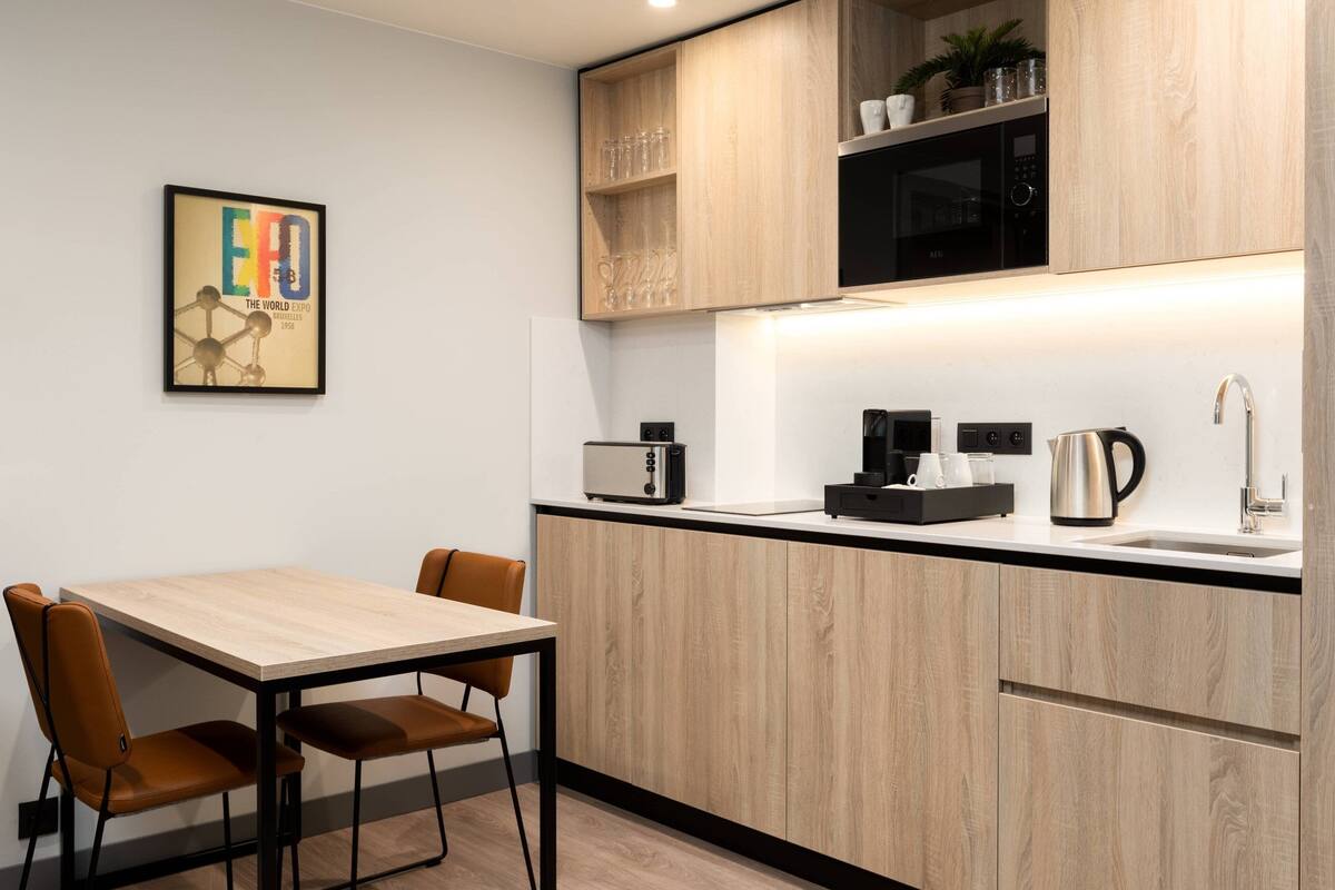 Eine moderne Küche mit Holzarbeitsplatte, einer Mikrowelle, einem Wasserkocher und einer Kaffeemaschine. An der Wand hängt ein gerahmtes Bild und es gibt einen Esstisch mit Stühlen.