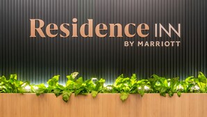Una zona de recepción con una pared oscura, un mostrador de madera y plantas verdes.