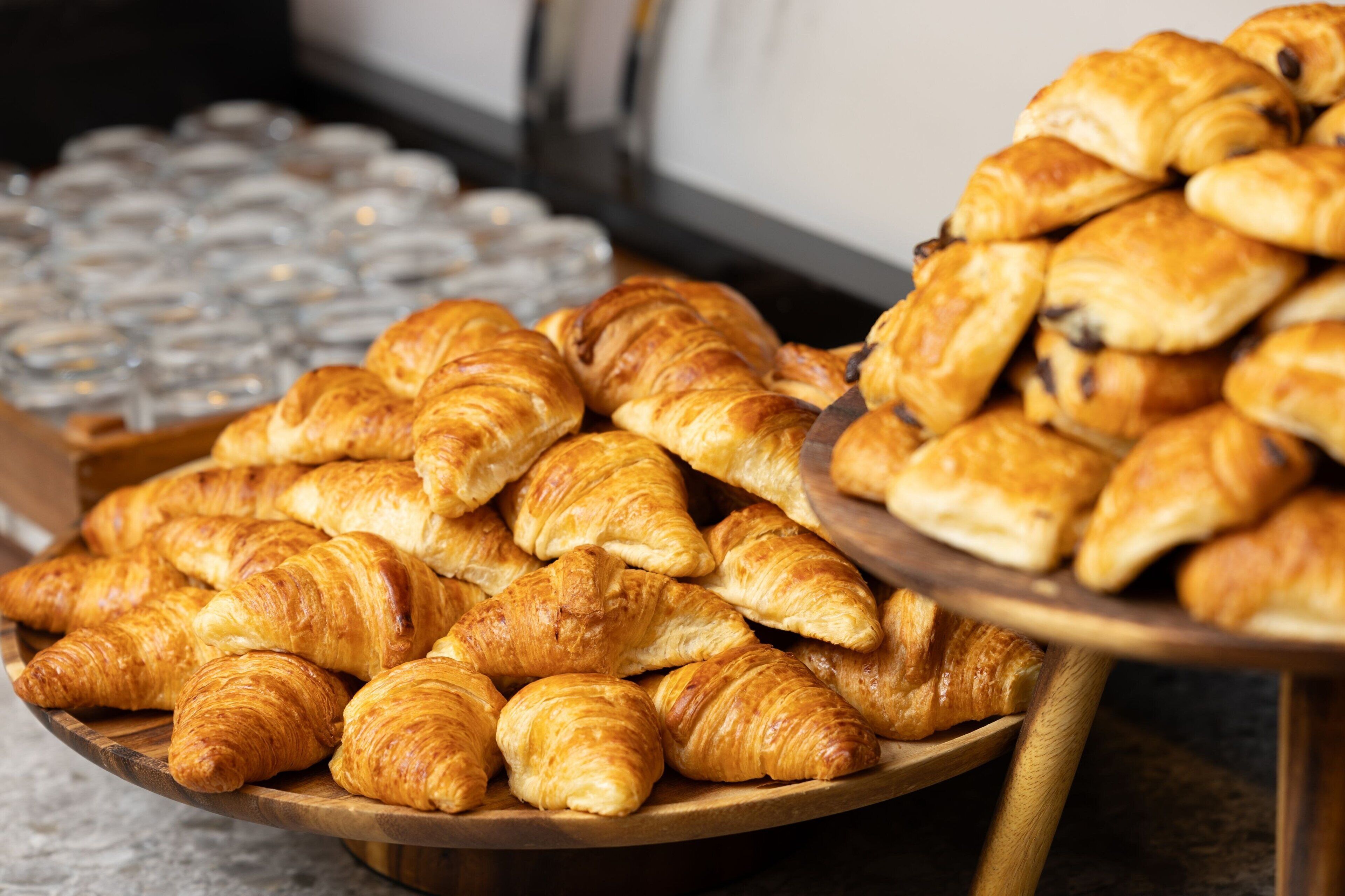 A wooden tray filled with assorted pastries, including croissants and chocolate-filled pastries, placed on a table.