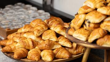 A wooden tray filled with assorted pastries, including croissants and chocolate-filled pastries, placed on a table.