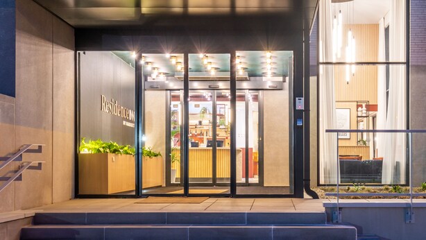 Entrada de hotel con mostrador de recepción, una escalera y una puerta de cristal que da al interior.