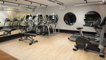 Een sportschool met loopbanden, elliptische trainers en een bank.