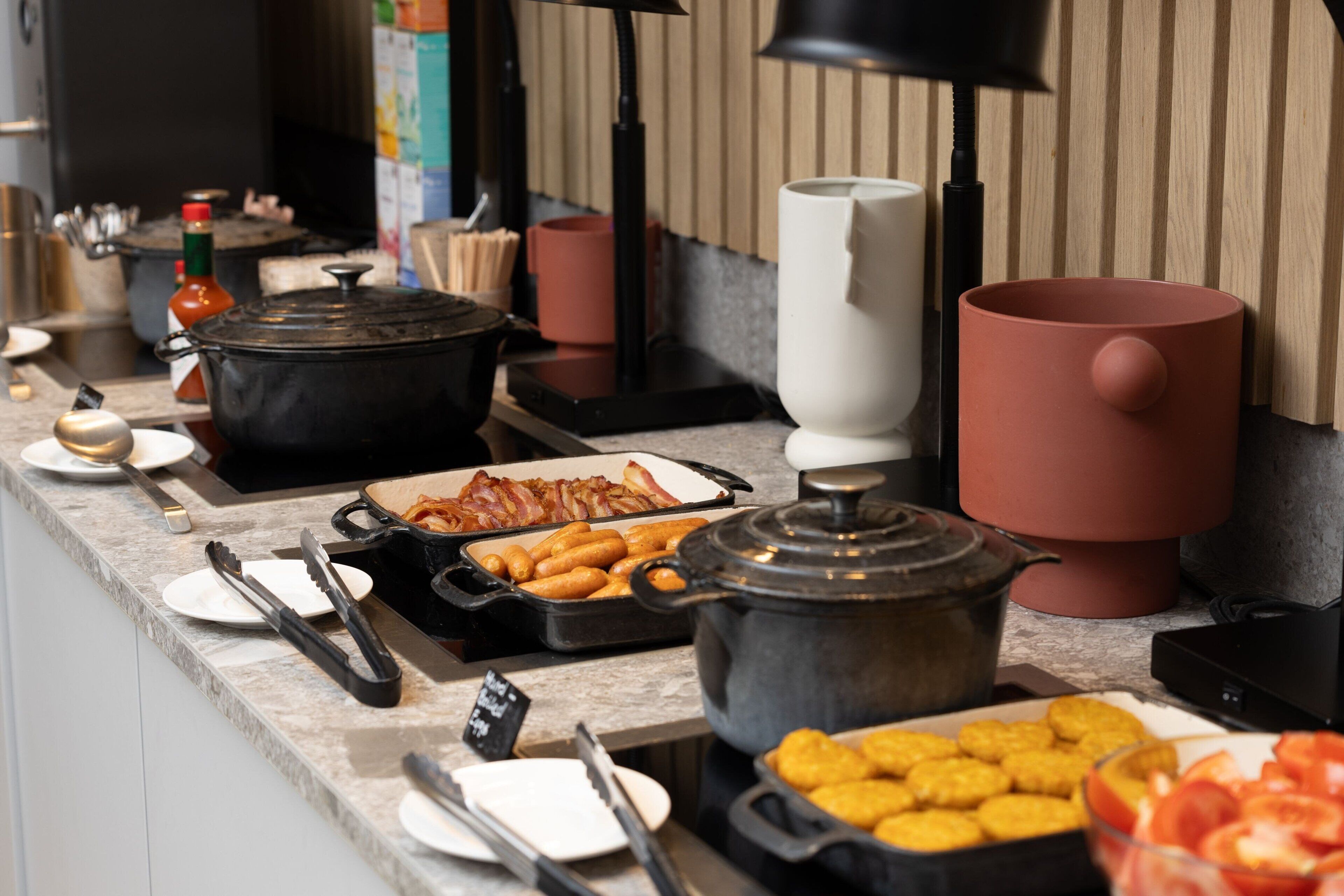 Balcão de buffet com diversos alimentos, incluindo uma panela de sopa, uma bandeja de bacon e uma tigela de frutas.
