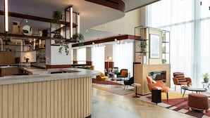 Un moderno vestíbulo de hotel con una zona de bar central, arreglos de asientos y grandes ventanales que dejan entrar luz natural.