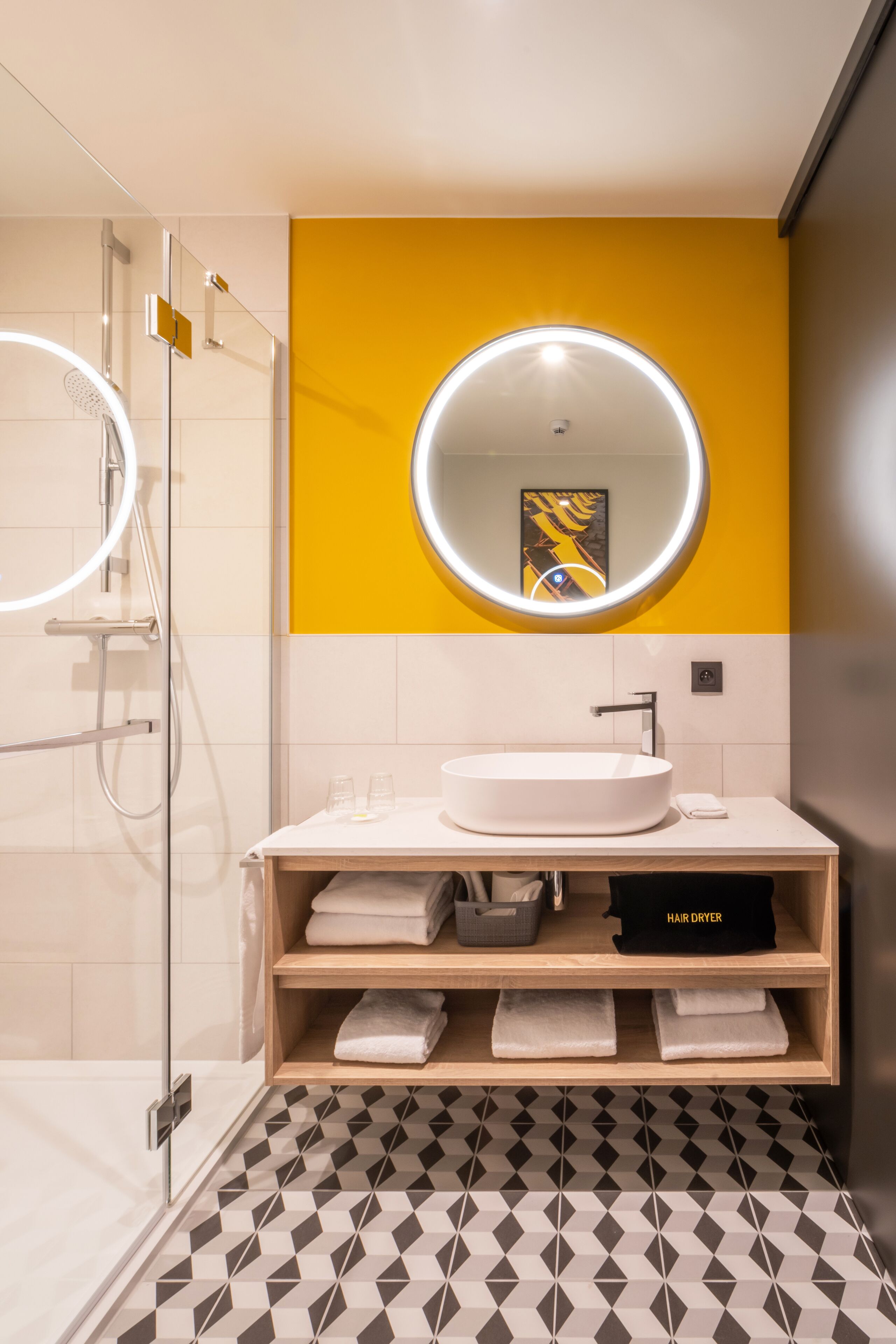 A modern bathroom with a glass-enclosed shower, a white sink, and a yellow accent wall.