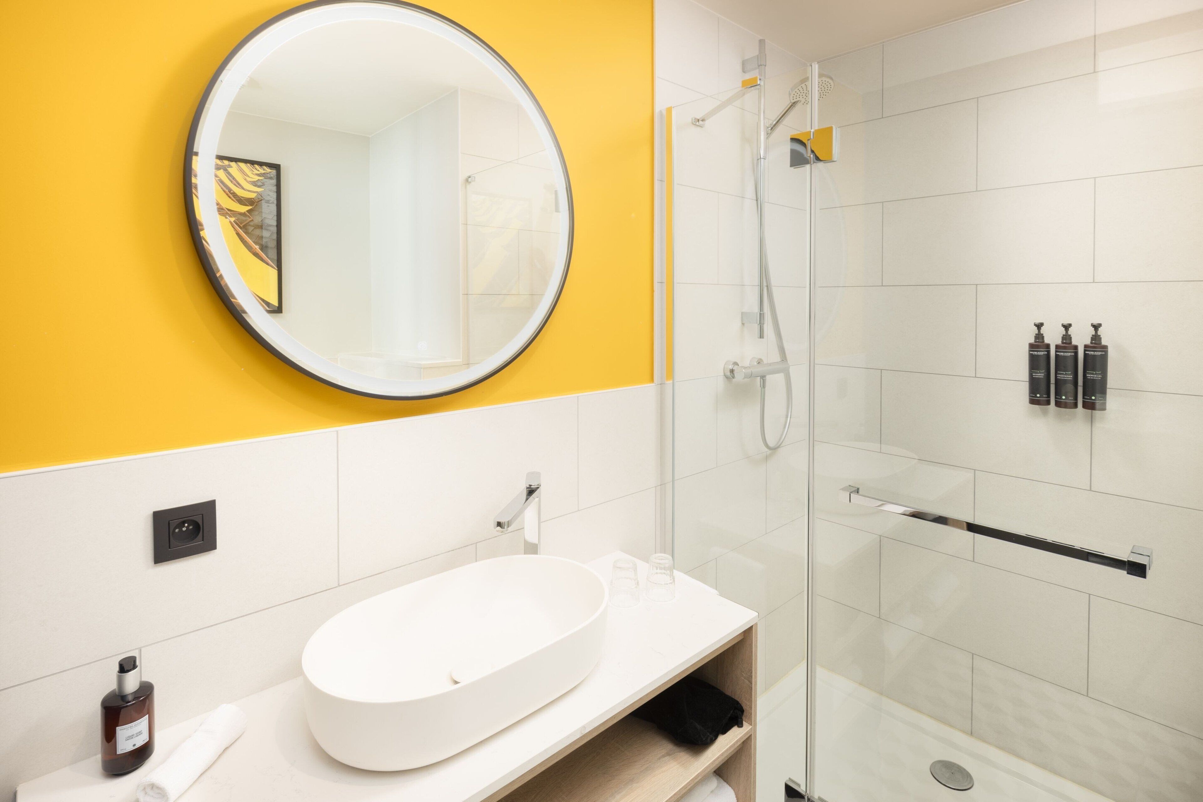 Un baño moderno con un espejo redondo, un lavamanos blanco y una ducha con cerramiento de vidrio.