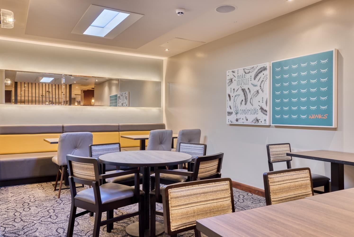 A modern hotel room with a seating area, a round table, and two wall art pieces.
