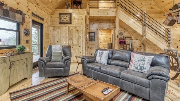 L’intérieur d’un chalet en bois comprend un escalier, des canapés en cuir, une table basse et un meuble en bois.