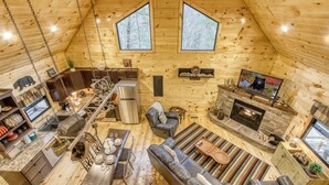 L’intérieur d’un chalet en bois comprend une cuisine, un coin repas, un salon, une cheminée et de grandes fenêtres.