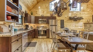 Une cuisine aménagée dans une maison en rondins, avec un coin repas, des appareils électroménagers en acier inoxydable et une grande fenêtre.