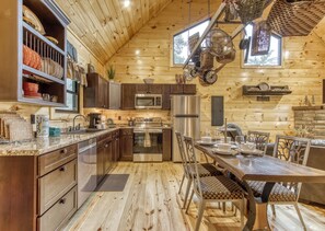 A log cabin kitchen with a dining area, stainless steel appliances, and a large window.