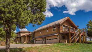 A two-story log cabin with a covered front porch and a garage. - Wrap Around Deck | Unmatched Views | Air Conditioning | STR2025-060 (Ridgway)